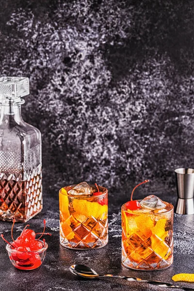 Old fashioned cocktail with cherries and orange twist.