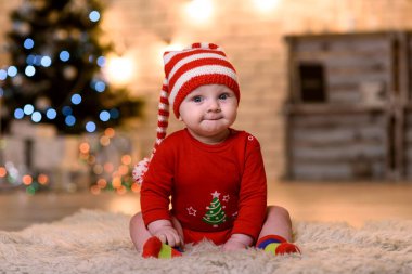 Yeni yıl elbisesi giymiş bir çocuk yere oturur ve gülümser.