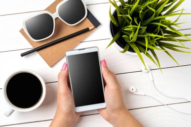 Beyaz ahşap masa üzerinde beyaz akıllı telefon kullanan kadın. Yakın çekim