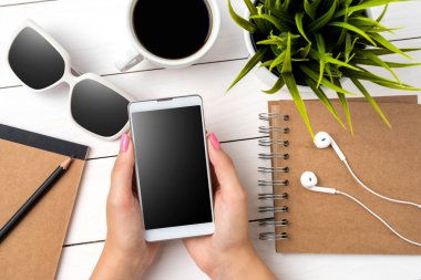 Beyaz ahşap masa üzerinde beyaz akıllı telefon kullanan kadın. Yakın çekim