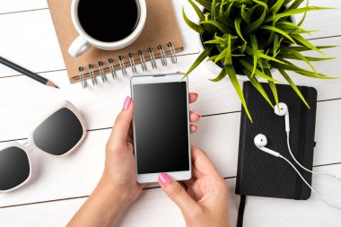 Beyaz ahşap masa üzerinde beyaz akıllı telefon kullanan kadın. Yakın çekim