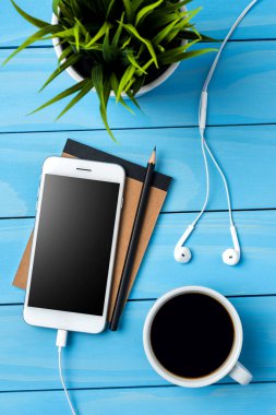 Beyaz akıllı telefon aksesuar ve mavi ahşap masa üzerinde yeşil bitki