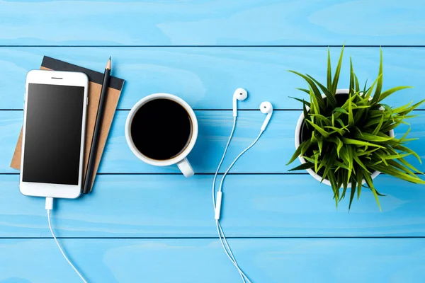 Beyaz akıllı telefon aksesuar ve mavi ahşap masa üzerinde yeşil bitki