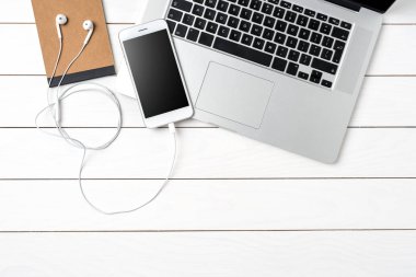 Beyaz akıllı telefon, dizüstü bilgisayar ve aksesuarları Beyaz ahşap masa üzerinde. Üstten görünüm