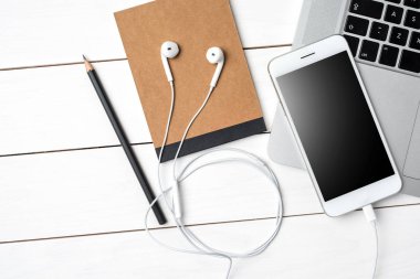 Beyaz akıllı telefon, dizüstü bilgisayar ve aksesuarları Beyaz ahşap masa üzerinde. Üstten görünüm