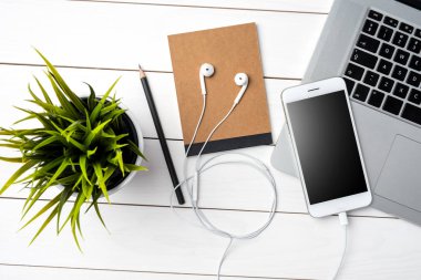 Beyaz akıllı telefon, dizüstü bilgisayar ve aksesuarları Beyaz ahşap masa üzerinde. Üstten görünüm