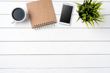 Smartphone, fincan kahve, notbook ve beyaz tahta masada yeşil bitki