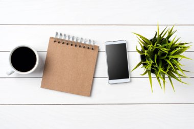 Smartphone, fincan kahve, notbook ve beyaz tahta masada yeşil bitki