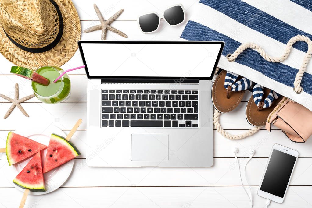 Online summer preparations concept with modern laptop, beach bag and accessories