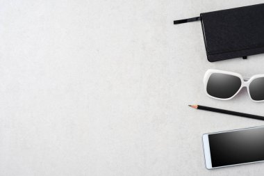 Modern smartphone, güneş gözlüğü, Not defteri ve kalem taş masada. Üstten görünüm