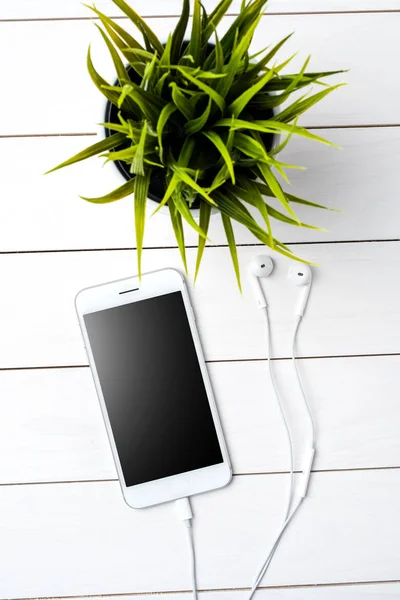 Modern smartphone with earphones on white wooden background