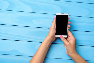 Mavi ahşap masa üzerinde beyaz akıllı telefon kullanan kadın