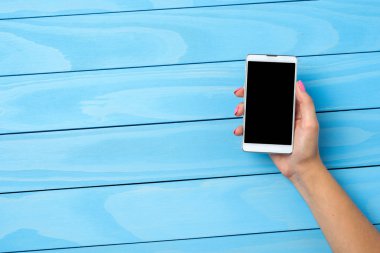 Mavi ahşap masa üzerinde beyaz akıllı telefon kullanan kadın