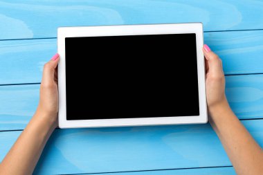 Beyaz dijital tablet mavi ahşap masa üzerinde tutan kadın