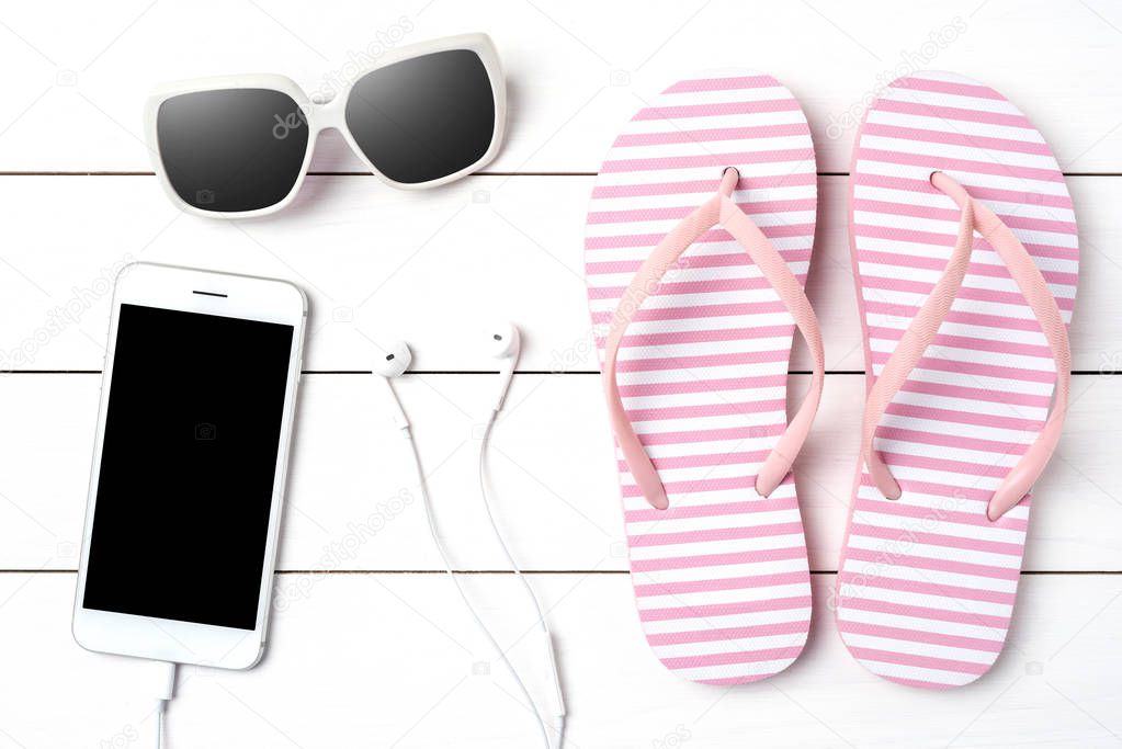 Pink flip flops with summer accessories on white wooden background