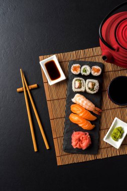 Wasabi 'li suşi, soya sosu ve siyah taştan arka planda çaydanlık.