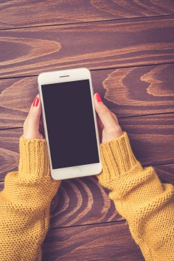 Eller sıcak kazaklı beyaz akıllı telefon tutarak. Yakın çekim