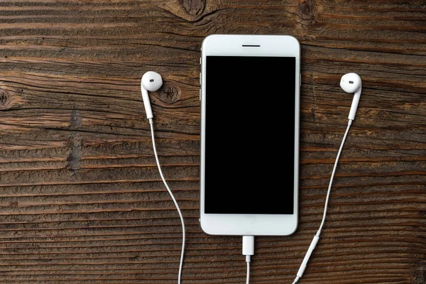 Modern smartphone with earphones on an old wooden background