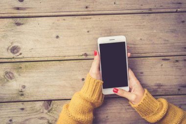 Sıcak süveterin içinde beyaz bir akıllı telefon kullanan kadın