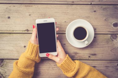 Sıcak süveterin içinde beyaz bir akıllı telefon kullanan kadın