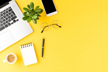 Ofis masaüstü. Sarı arka planda iş aksesuarları olan zarif bir laptop.
