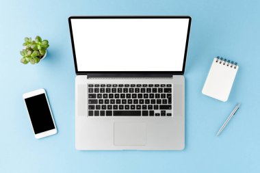 Boş ekran ve mavi arka planda iş aksesuarları olan bir dizüstü bilgisayar görüntüsü. Ofis masaüstü. Düz yatıyordu