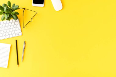 Sarı arka planda iş aksesuarları ve kopyalama alanı olan şık bir ofis masası. Üst görünüm