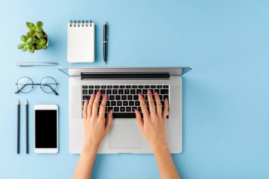 Mavi masadaki aksesuarlı dizüstü bilgisayarı kullanan kadın elleri. Kopyalama alanı ile iş geçmişi. Üst görünüm