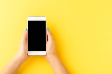 Sarı arka planda boş ekranı olan cep telefonu kullanan kadın elleri. Üst görünüm