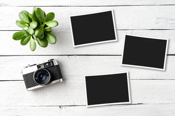 Empty picture frames with photo camera on white wooden table. Top view