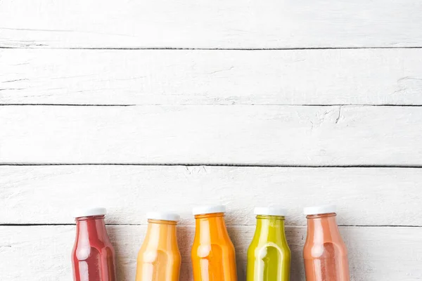 Fresh fruit and vegetable juices in bottles on white wooden background with copyspace