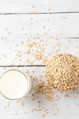 Beyaz ahşap zemin üzerinde bir bardak yulaf sütü ve kâsede yulaf ezmesi.