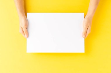 Sarı masanın üzerinde boş kağıt çarşaf tutan kadın elleri. Kapat.