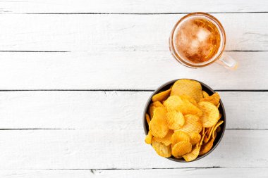 Bir bardak bira ve patates cipsi ahşap masada kasede.