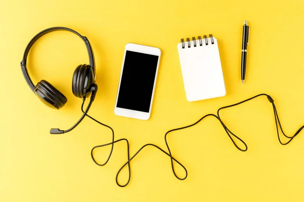 带电话 笔记本和钢笔的服务台耳机放在黄色桌面上 呼叫中心 — 图库照片