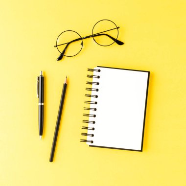 Sarı masada boş kalemler ve gözlüklerle dolu bir defter. Ofis masaüstü