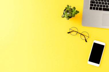 Sarı arka planda iş aksesuarları ve kopyalama alanı olan şık bir ofis masası. Üst görünüm
