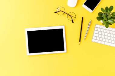 İş aksesuarlarıyla sarı arka planda boş ekranı olan dijital tablet. Ofis masaüstü
