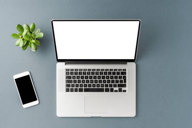 Boş ekranlı dizüstü bilgisayar ve gri masada akıllı telefon. Ofis masaüstü. Üst görünüm