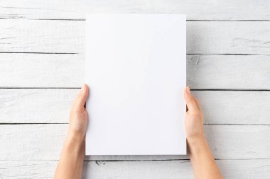 Beyaz ahşap zemin üzerinde boş kağıt çarşaf tutan kadın eller. Üst görünüm