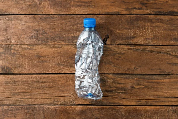 Used and crushed small bottle of water on rustic wooden background. Plastic recycling. Top view