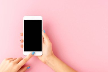 Mavi tırnaklı, elinde cep telefonu olan, pembe arka planda boş ekranlı bir kadın eli. Üst görünüm