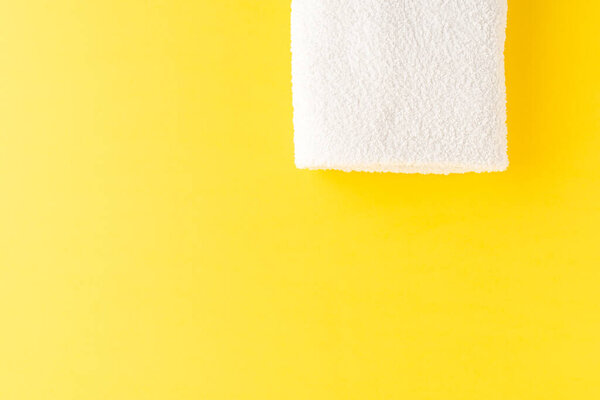 Overhead shot of clean bath towel on yellow table with copyspace
