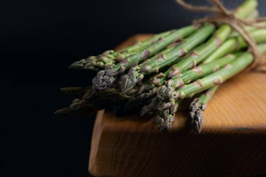 Koyu arkaplanda tahta üzerinde bir demet kuşkonmaz. yatay oryantasyon. ön görünüm