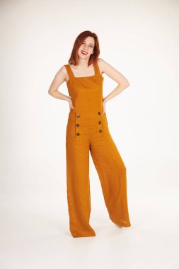 Beyaz arka planda turuncu tulumlu gülümseyen kızıl kız.