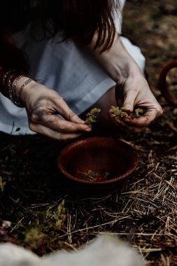 Beyaz cadı elbiseli bir kadın büyüler ve iksirler için seramik fırçayla kurutulmuş otları yırtıyor. Korku teması. Cadılar Bayramı.
