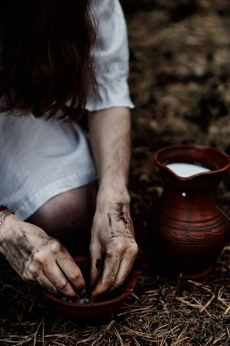 Beyaz cadı elbiseli bir kadın büyüler ve iksirler için seramik fırçayla kurutulmuş otları yırtıyor. Korku teması. Cadılar Bayramı.