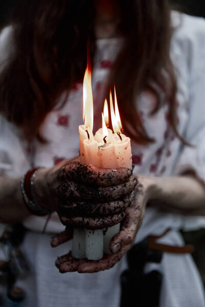 A girl in a white dress holds with dirty hands fire candles with flowing wax. Halloween theme.