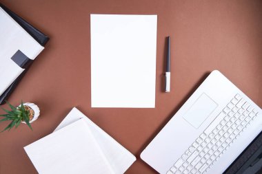 Kayıt için beyaz sayfası ve dizüstü bilgisayarı olan kahverengi bir ofis masası. Yukarıdan bak. Ticari aksesuarları olan düz bir ev..