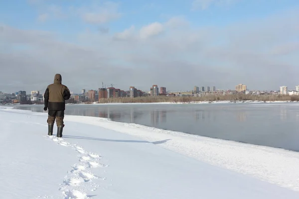 Tall man in warm clothes walking along the snowy bank of a frozen river, Ob River, Russia